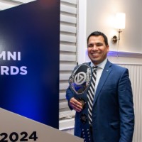 Victor Cardenas poses with his award in front of GVSU Alumni Awards sign